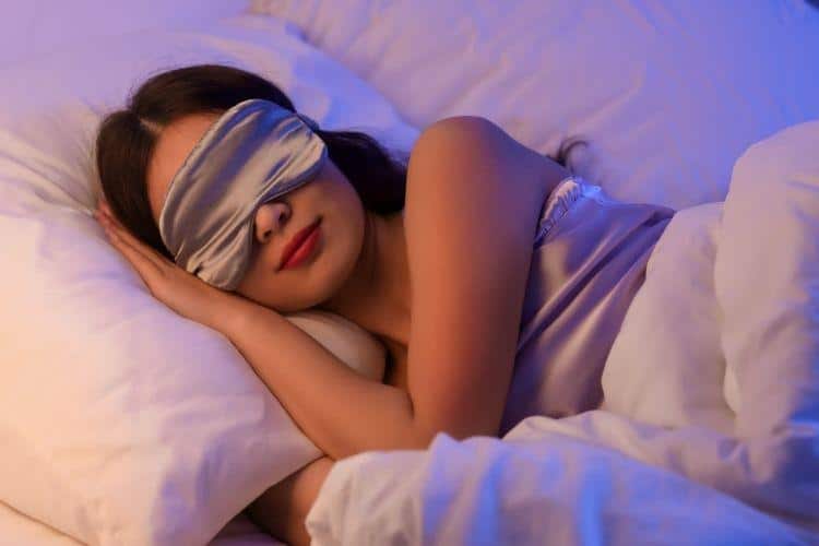 Beautiful Young Woman with Sleep Mask Sleeping in Bed