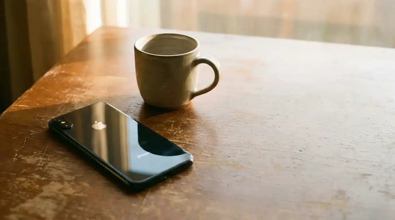 Ceramic mug and smartphone on wooden table in warm natural light
