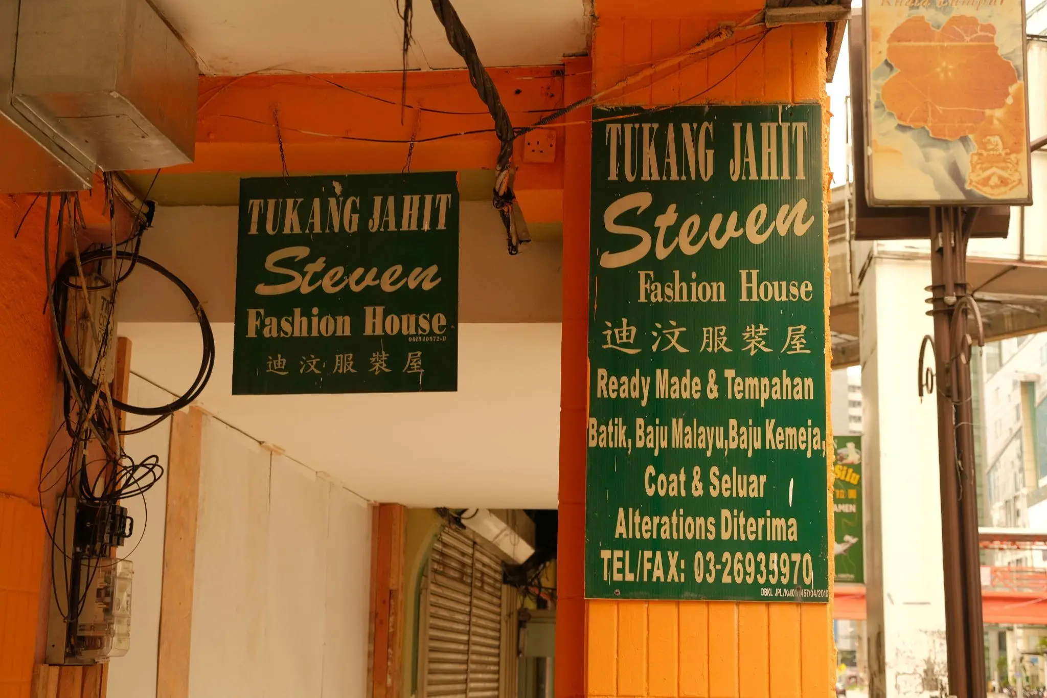 Tailor shop signs with text under an orange ceiling, visible wiring and fixtures