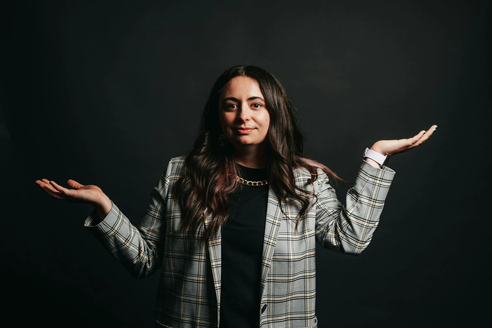 Woman in plaid blazer with arms raised against dark background