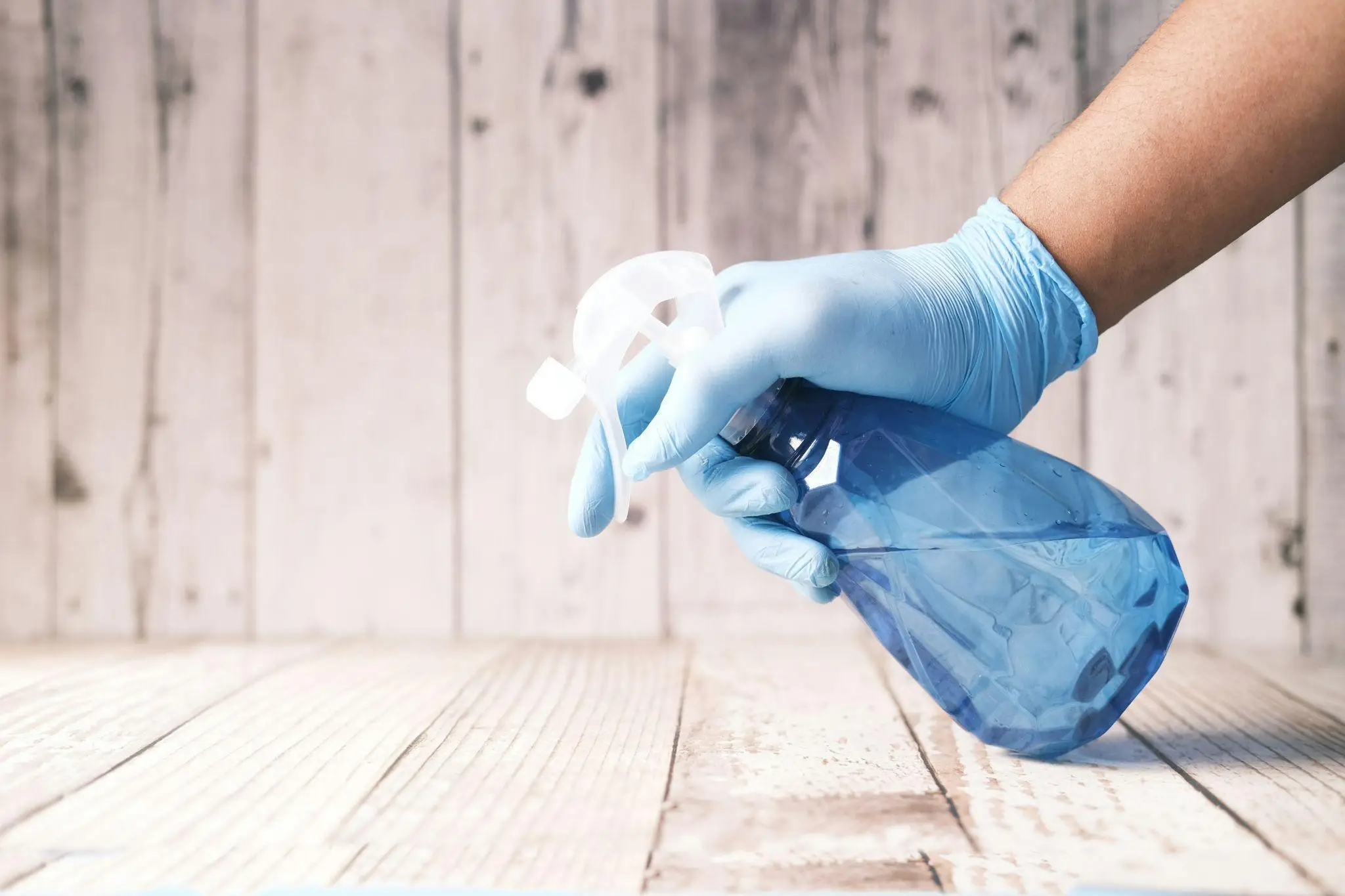 Hand in blue glove holding spray bottle against wooden background