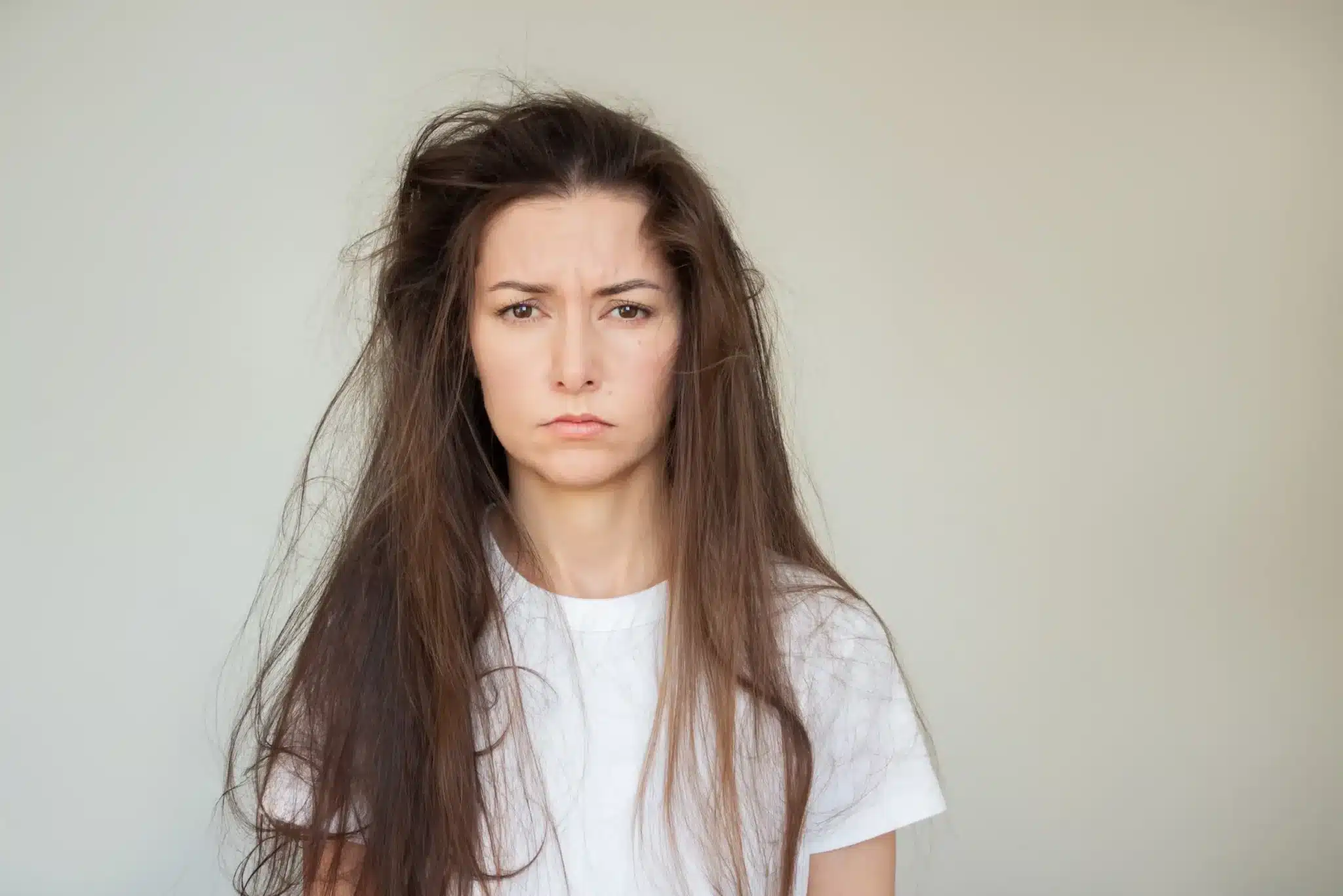 Woman with tousled hair and serious expression wearing white t-shirt against neutral background