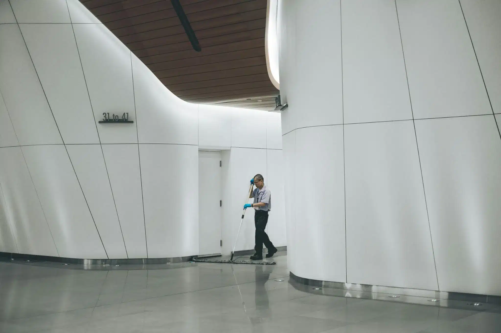 Person mopping floor in modern hallway with curved white walls and overhead lighting