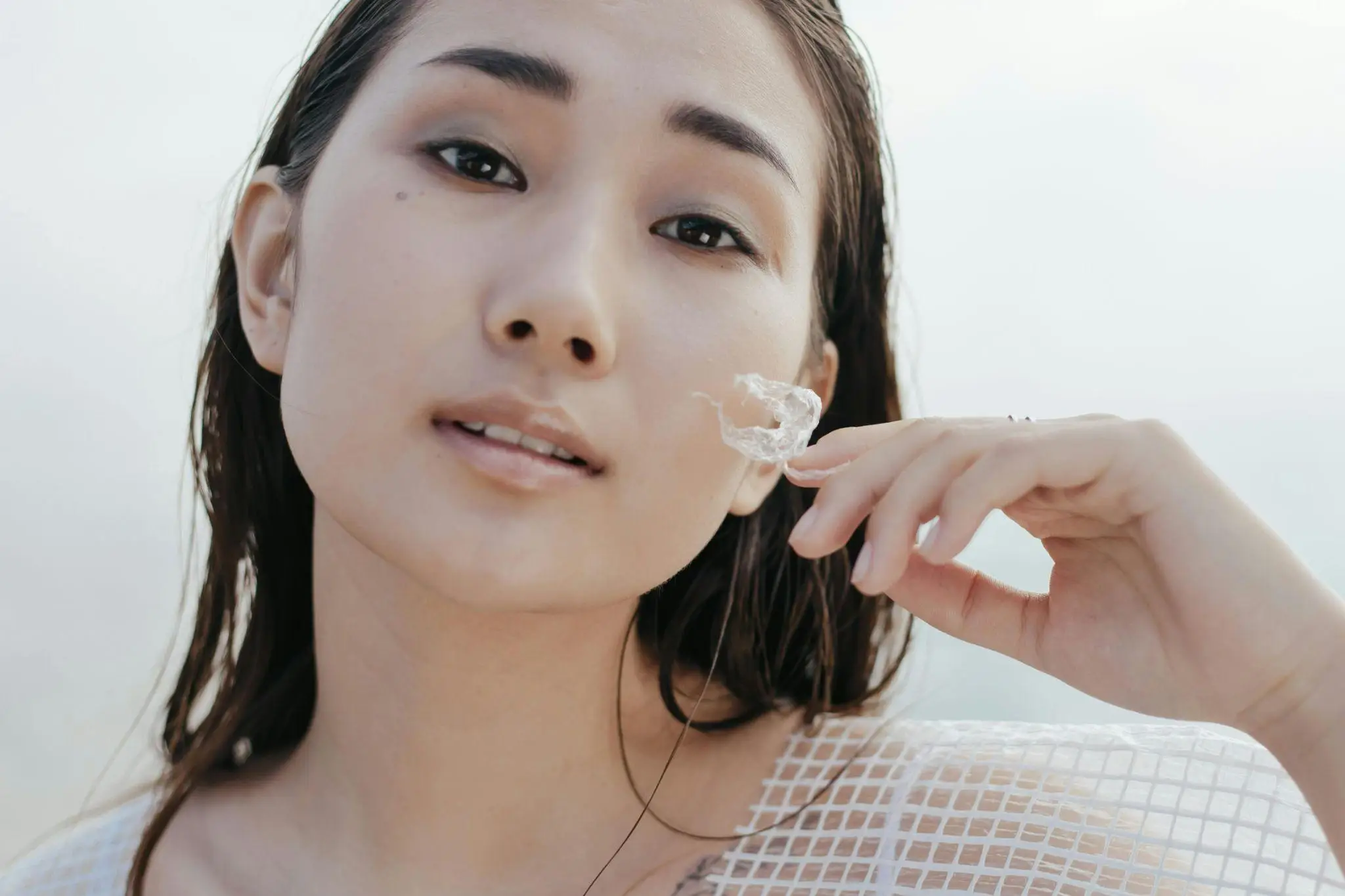 Person holding transparent object close to face with wet hair in bright setting