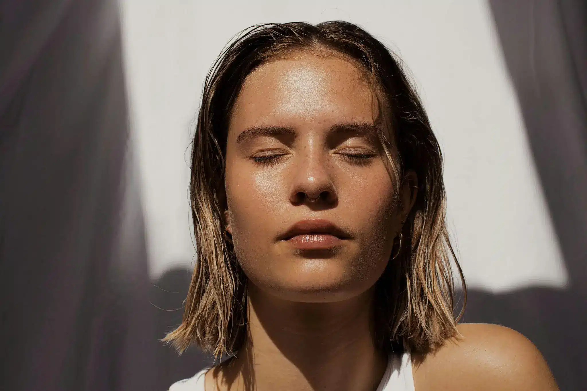 Close-up of a person with eyes closed, sunlit face, wearing a white shirt