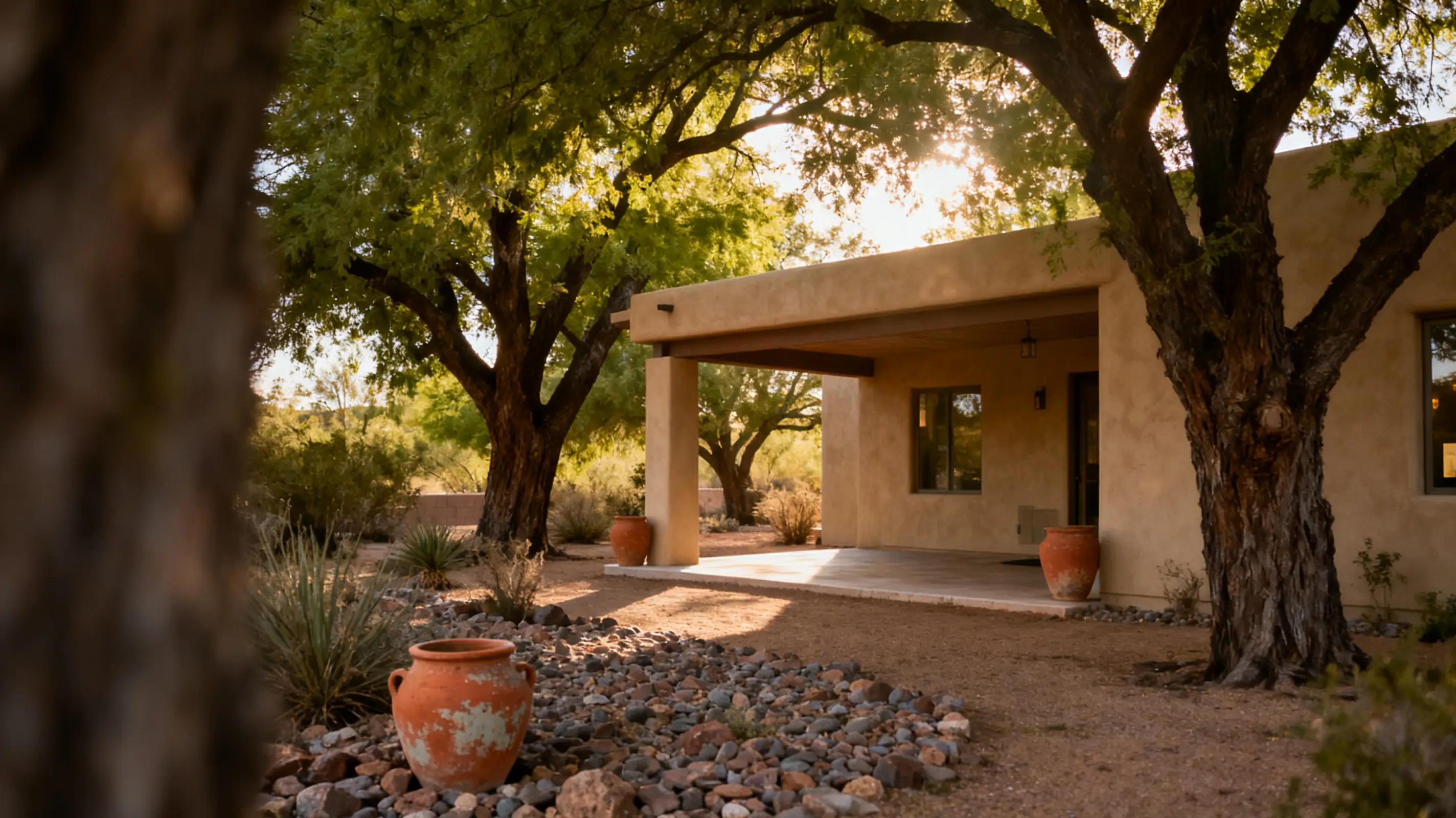 Rustic adobe house surrounded by desert landscape and trees in sunny setting