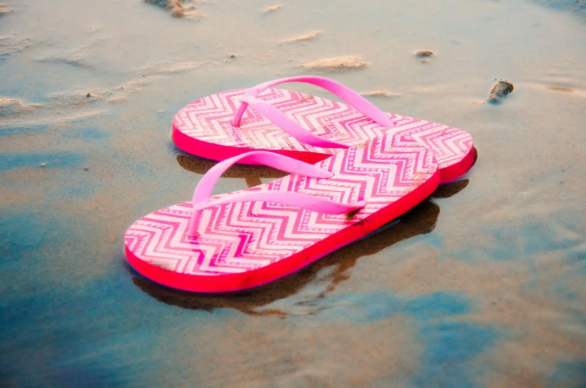 Pink flip-flops with chevron pattern on wet sandy beach