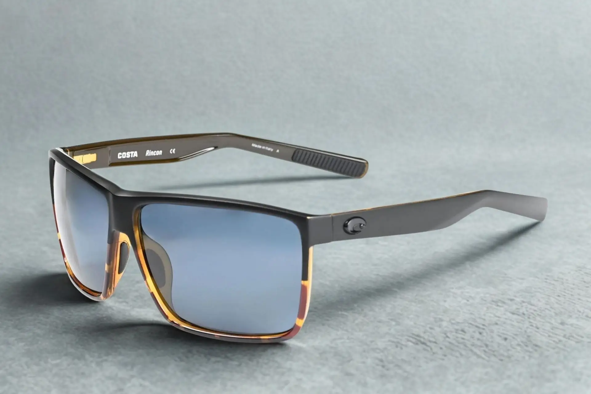 Rectangular tortoise-shell sunglasses with blue lenses on textured gray surface