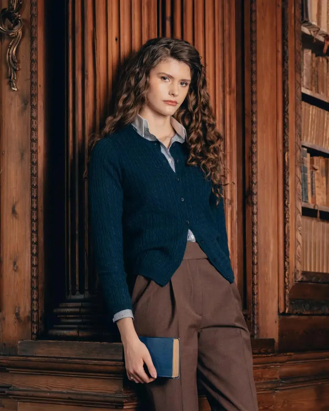Young woman in blue cardigan holding a book in a vintage library setting