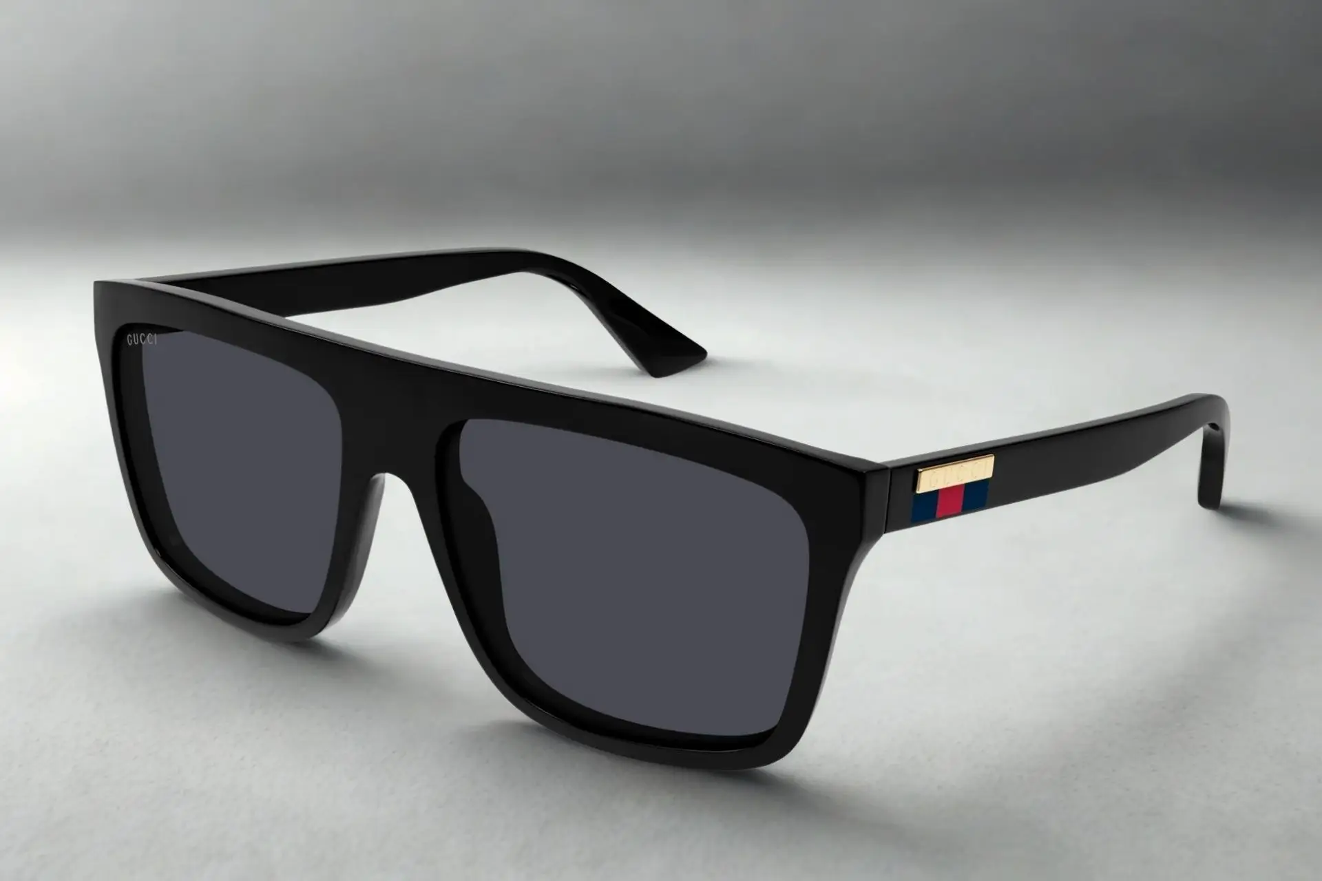 Black rectangular sunglasses with gold and colored temple logo on neutral background