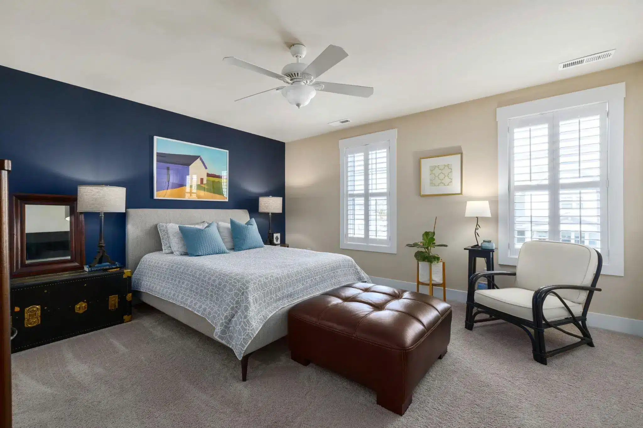 Bedroom with blue accent wall, upholstered bed, and brown leather ottoman in natural light