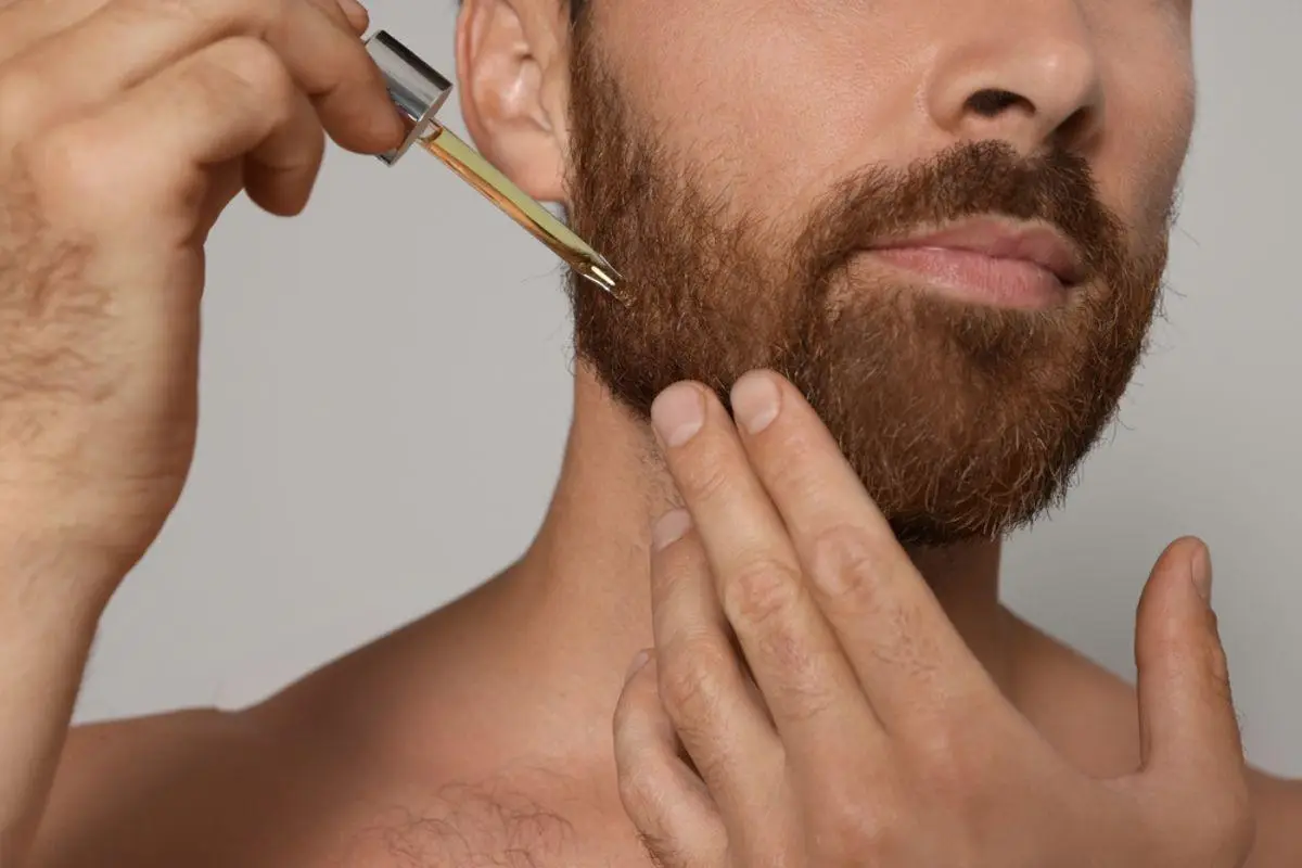 Man applying beard oil with dropper on cheek in neutral setting