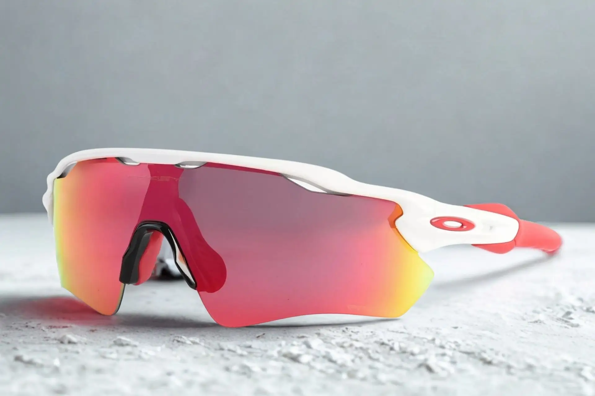 Sports sunglasses with red mirrored lenses and white frame on textured gray surface