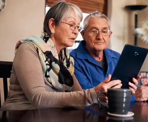 Elderly couple sitting at table using a tablet in a cozy living room setting