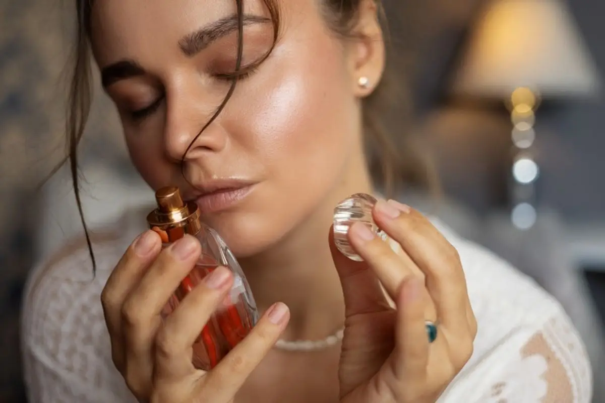 Woman holding perfume bottle with closed eyes in softly lit room