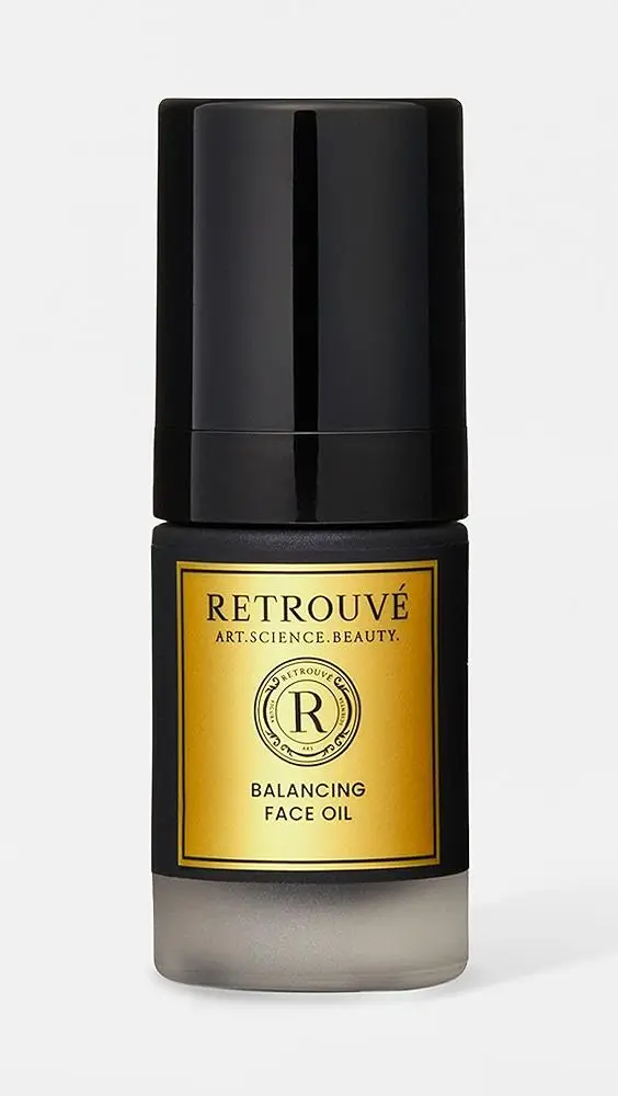 Dark glass bottle of balancing face oil with black cap and gold label on plain background