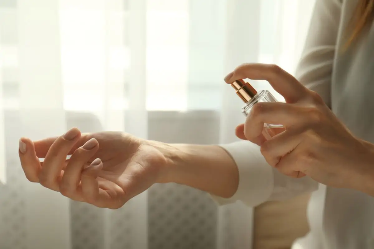 Person applying perfume to wrist in softly lit indoor setting