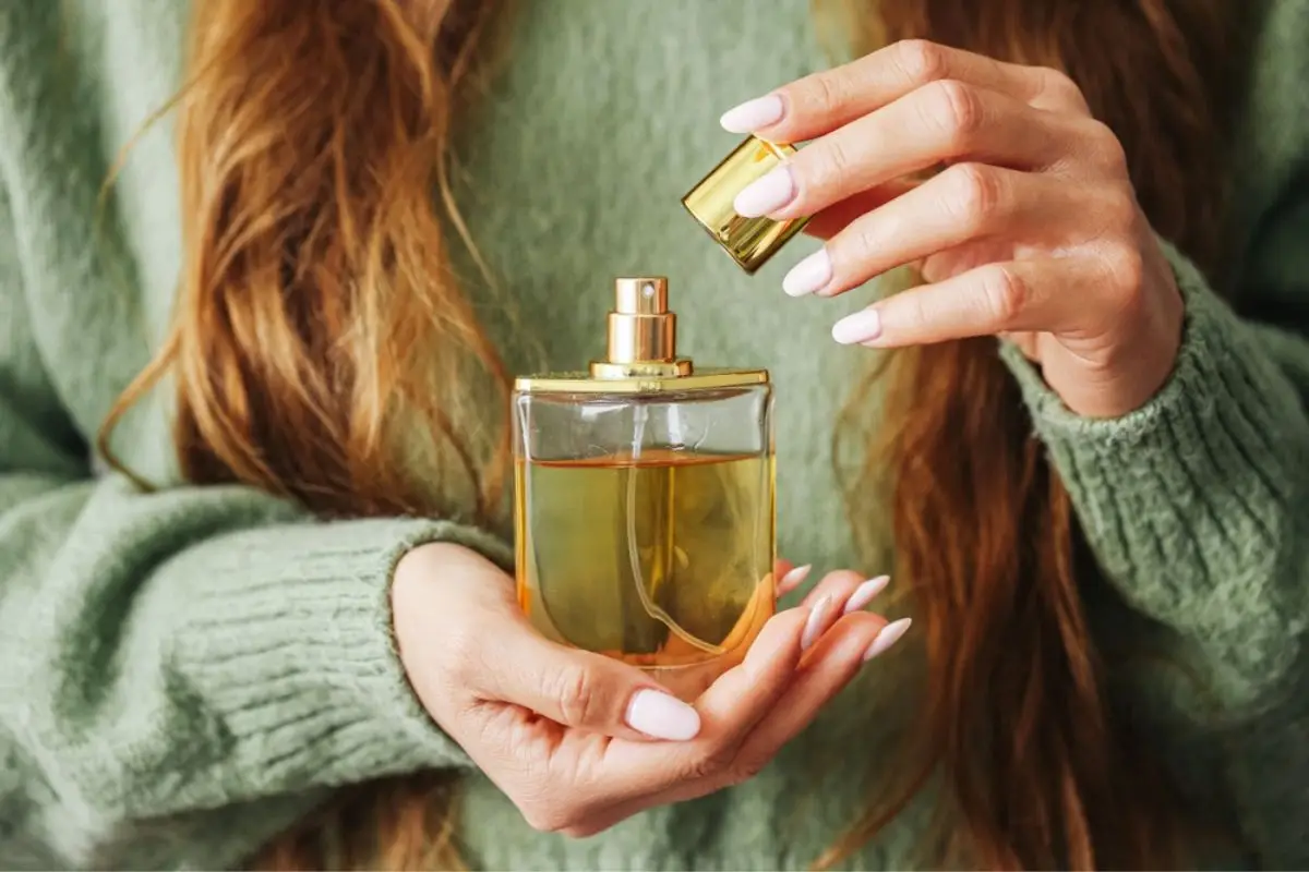 Hands holding a gold-capped perfume bottle in a cozy setting