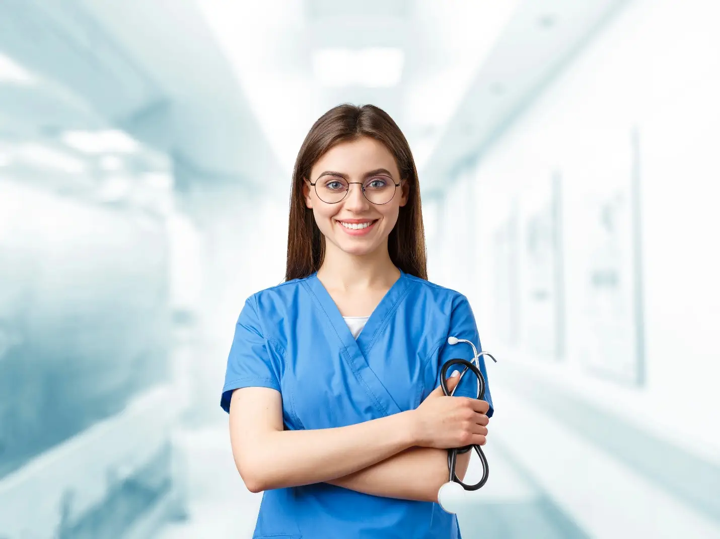 Smiling healthcare professional in blue scrubs holding stethoscope in bright hospital corridor