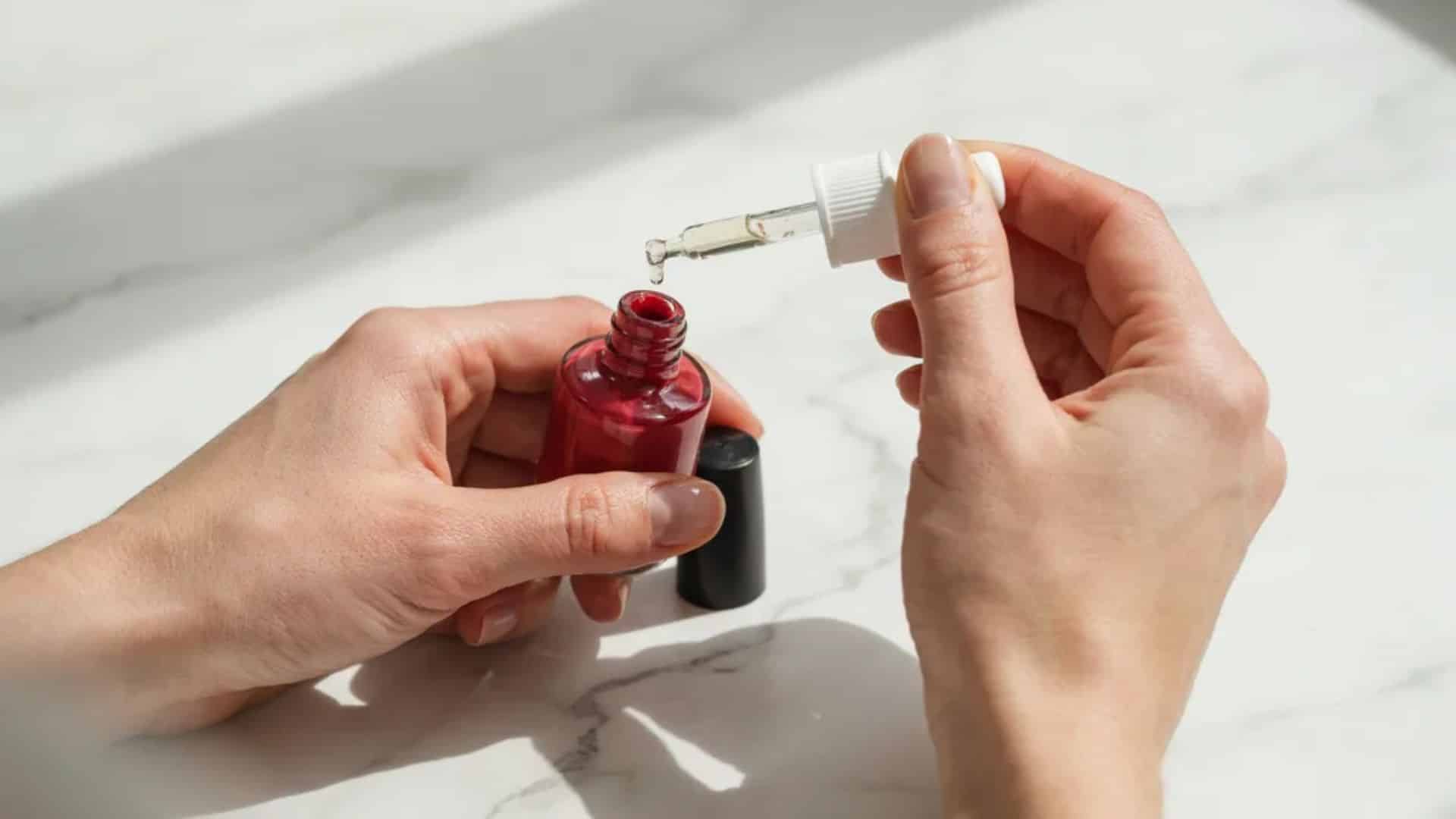 Adding nail polish thinner drops into thick deep cherry red nail polish to restore consistency
