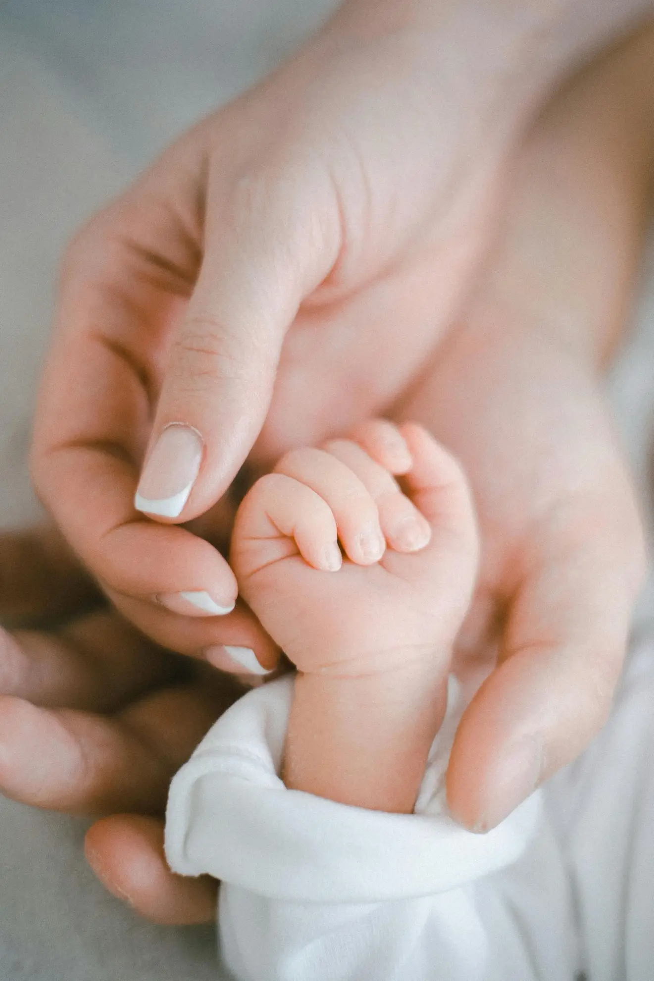 Adult hand gently holding a newborn's hand in a close-up shot