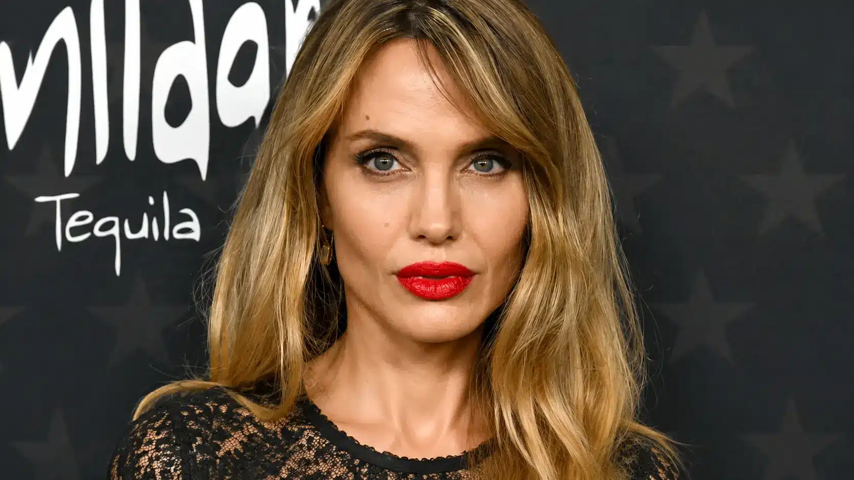 Close-up portrait of Angelina Jolie with red lipstick at a Milag Tequila event against a dark backdrop.
