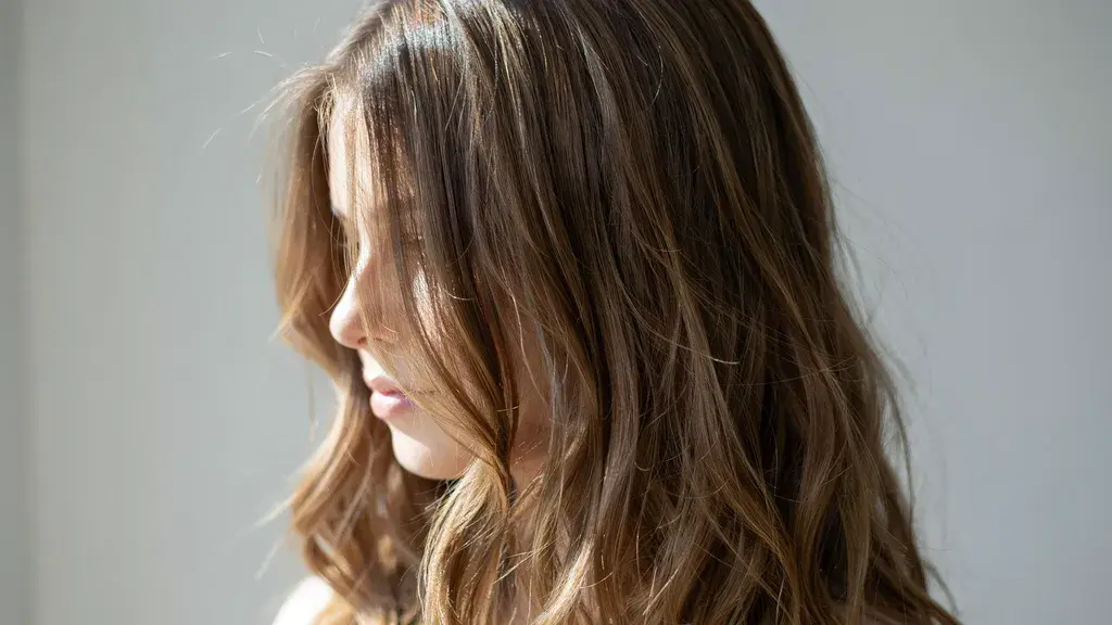 Soft brown hair with subtle highlights styled in loose waves showing layered texture and natural shine in bright light