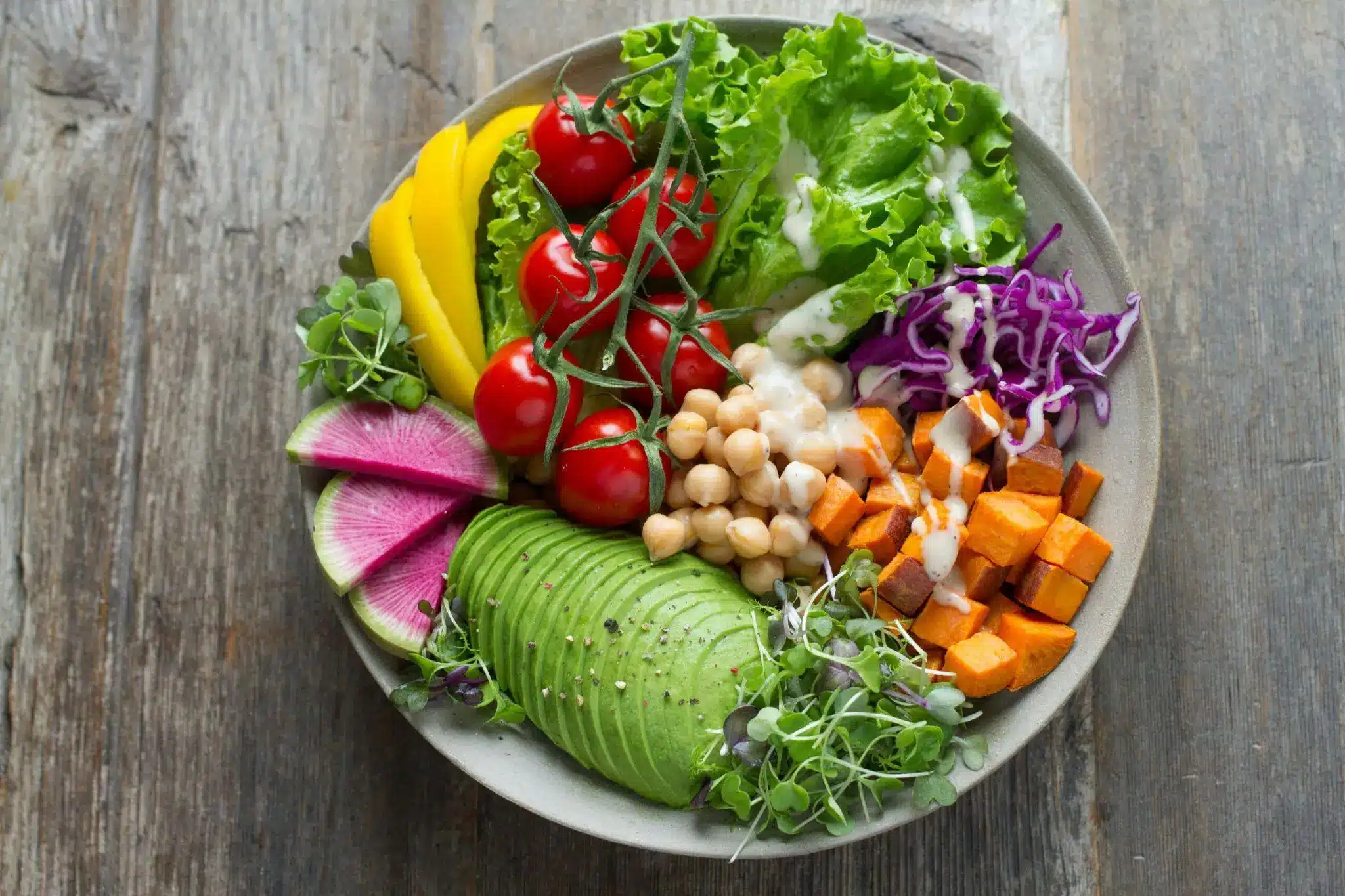 Colorful salad bowl with avocado, cherry tomatoes, lettuce, chickpeas, and sweet potatoes on wooden table