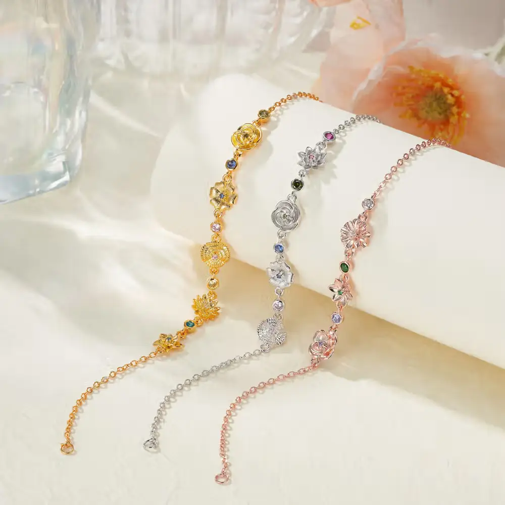 Gold, silver, and rose gold floral charm bracelets on white surface with flowers