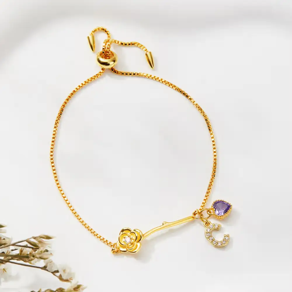 Gold bracelet with rose charm and gemstone on white background with dried flowers nearby