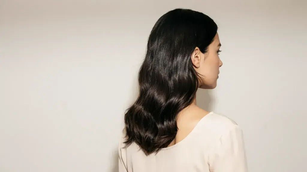 Woman with sleek black wavy hair showing a glossy dark hairstyle from a side profile view.