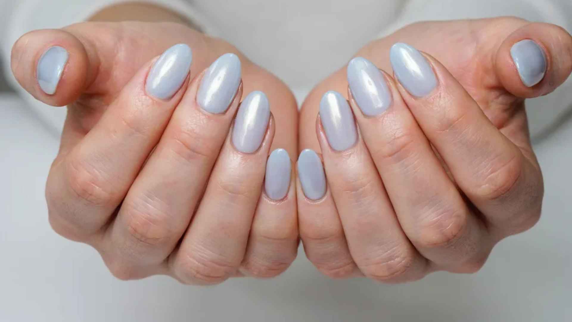 Close up of pale blue glazed donut nails with an icy pastel base and a smooth pearl chrome finish in soft light