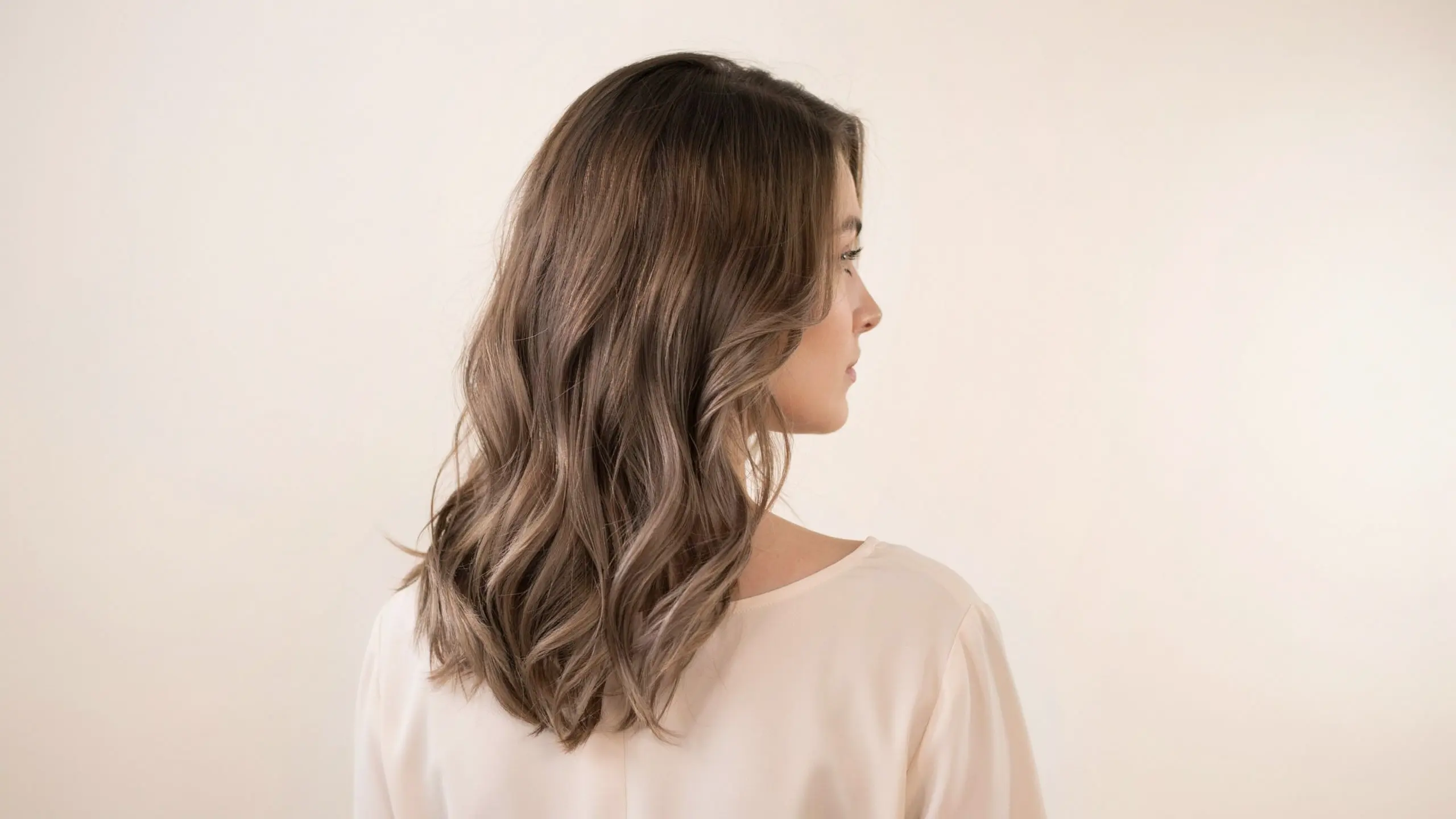 Woman with medium brown wavy hair featuring soft highlights and a layered hairstyle viewed from the side.