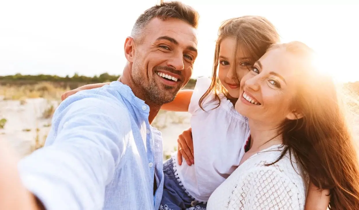 Family taking a selfie on a sunny beach with bright smiles