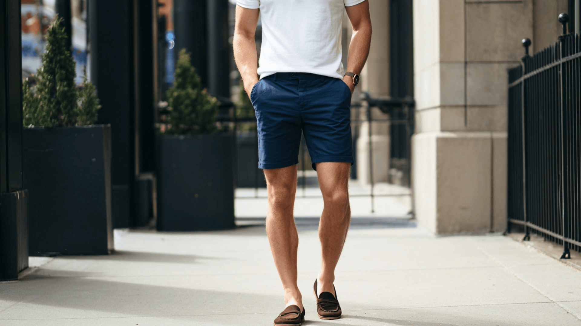 Man styling beige chino shorts with a t shirt and white sneakers for a smart casual summer look.