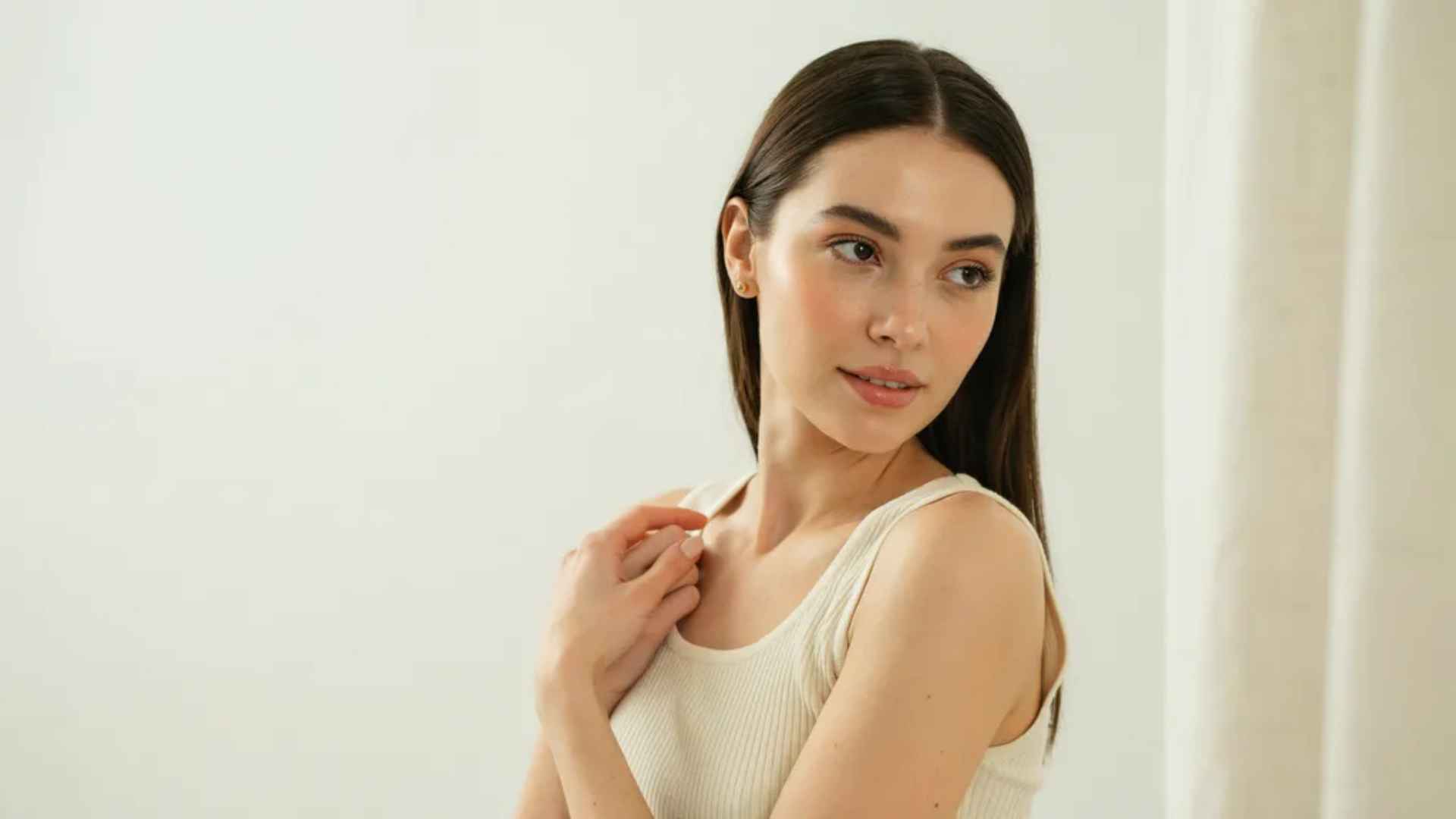 Woman showing a clean girl makeup look with fresh skin, groomed brows, rosy cheeks, and glossy lips