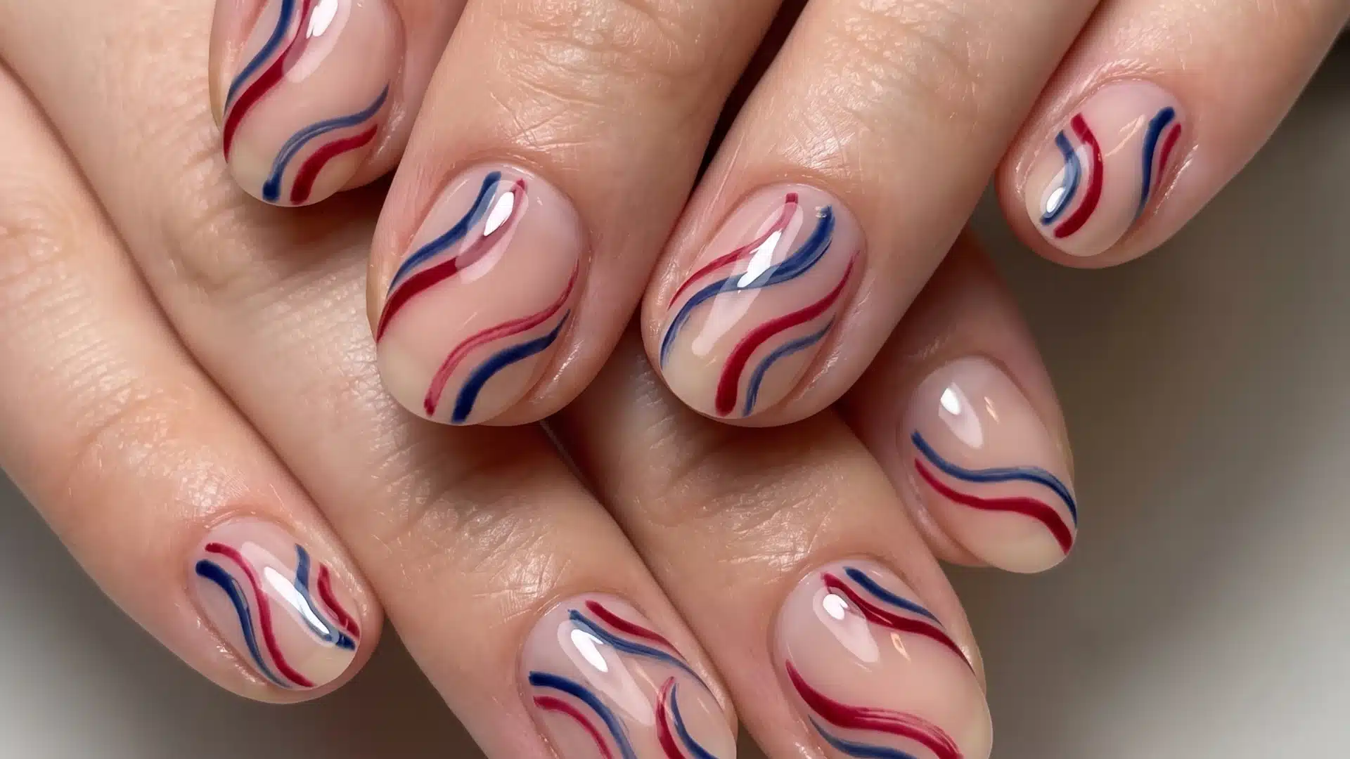 Hand showcasing minimalist wave nail art with glossy neutral nails and vibrant red and navy blue accents