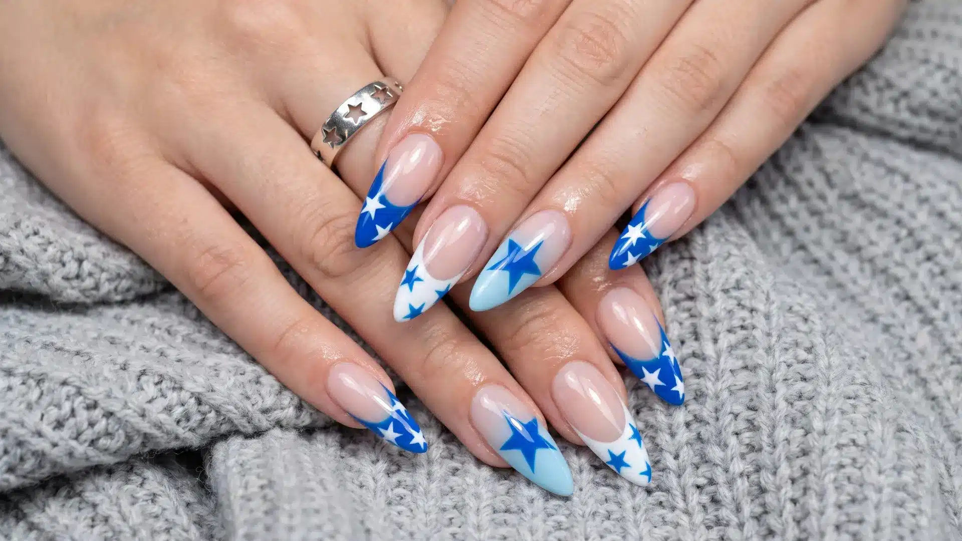 Festive nail design featuring translucent nude nails with vibrant blue star patterns and white accent details on tips
