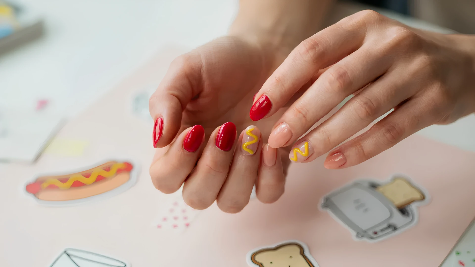 Artistic manicure showcasing bold red nails paired with yellow decorative lines and soft neutral nail accents on hands