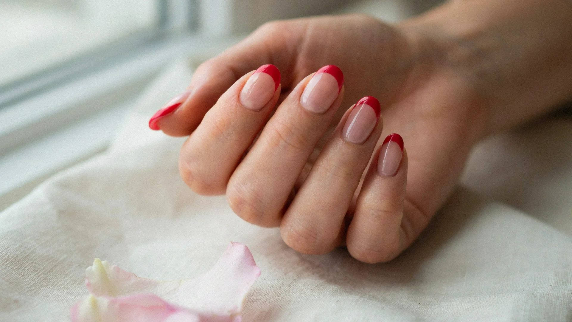 Minimal nail art featuring clean nude nails with vibrant red French tips displayed in a soft close up setting