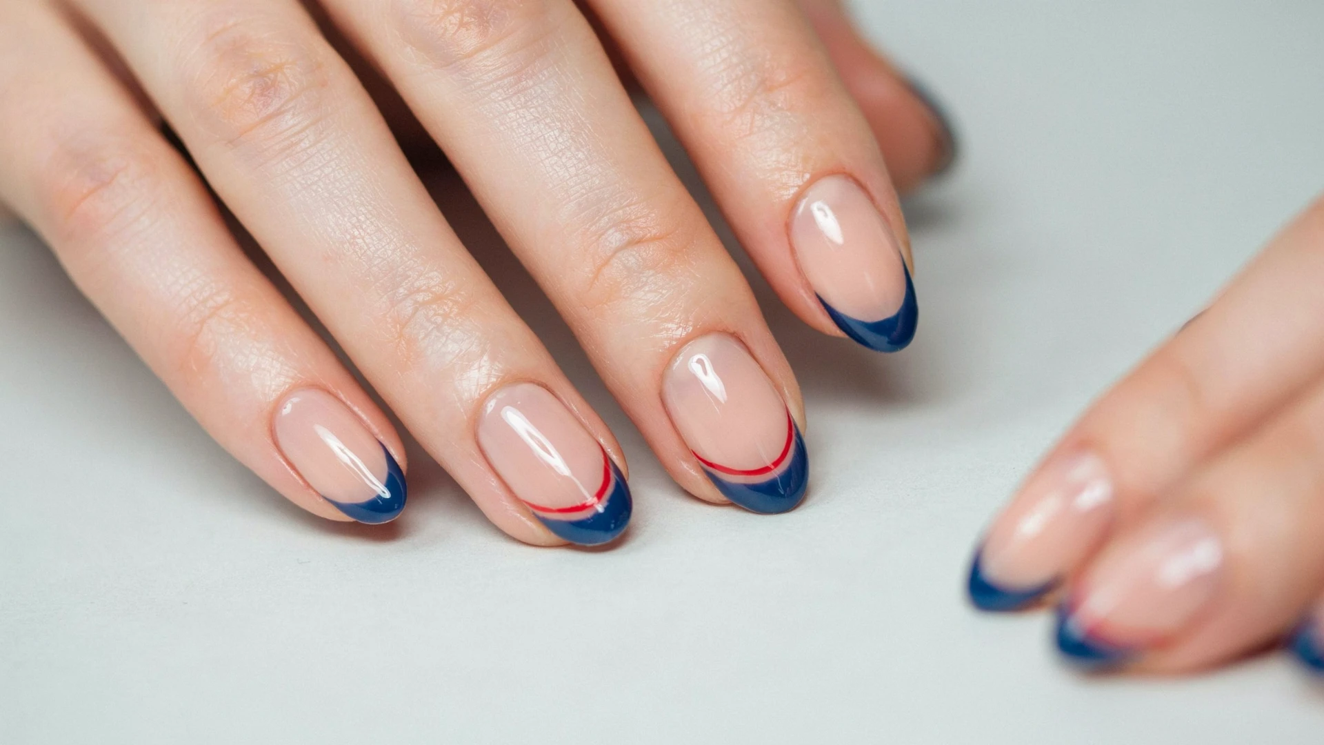 Minimal two tone manicure featuring glossy nude nails with blue French tips and small red accents for a chic look