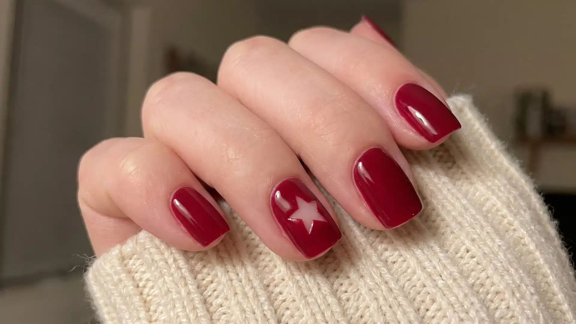 Close view of classic red manicure featuring a subtle star accent design and shiny rounded nails over knitted fabric background