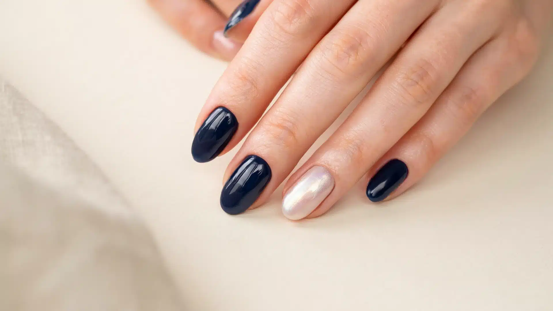 Modern manicure featuring rich navy blue polish with one luminous pearl finish nail and smooth glossy texture
