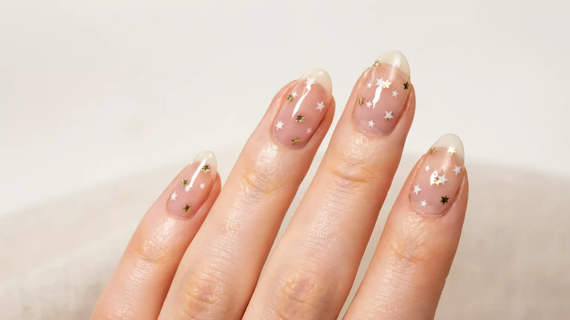 Soft neutral manicure featuring transparent pink nails with sparkling white and gold star embellishments