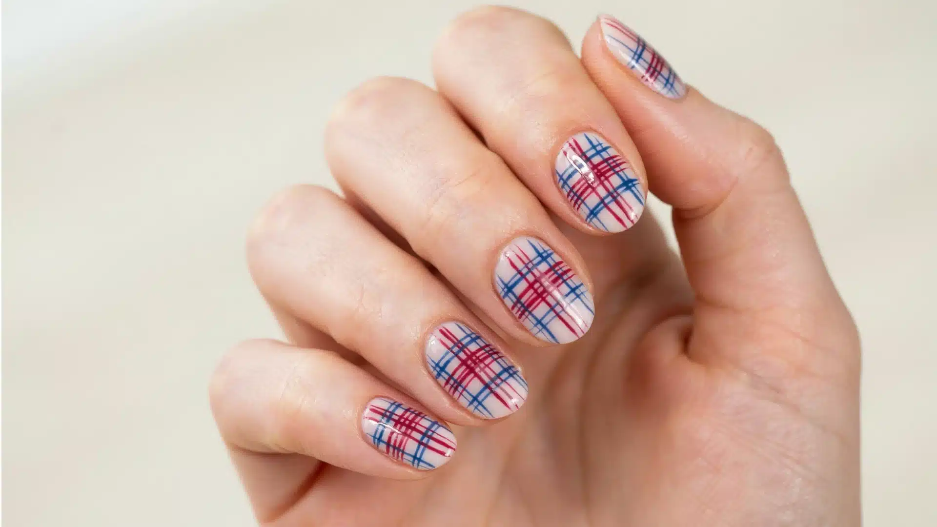 Close view of tartan inspired nail design featuring white nails with colorful red blue stripe patterns and glossy finish