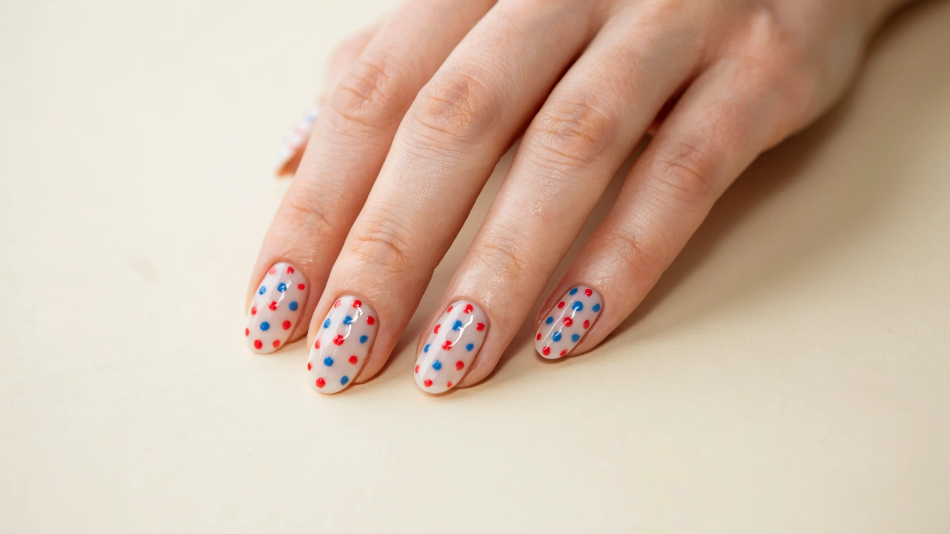 Fun patriotic inspired nail art featuring white nails with alternating red and blue polka dot decorations on a hand