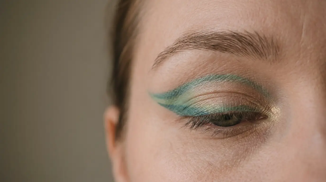 Close-up of an eye with intricate green eyeshadow design in neutral lighting
