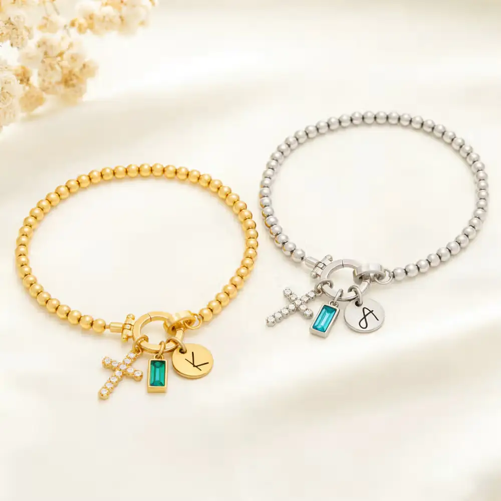 Gold and silver charm bracelets with cross and gemstone accents on cream background