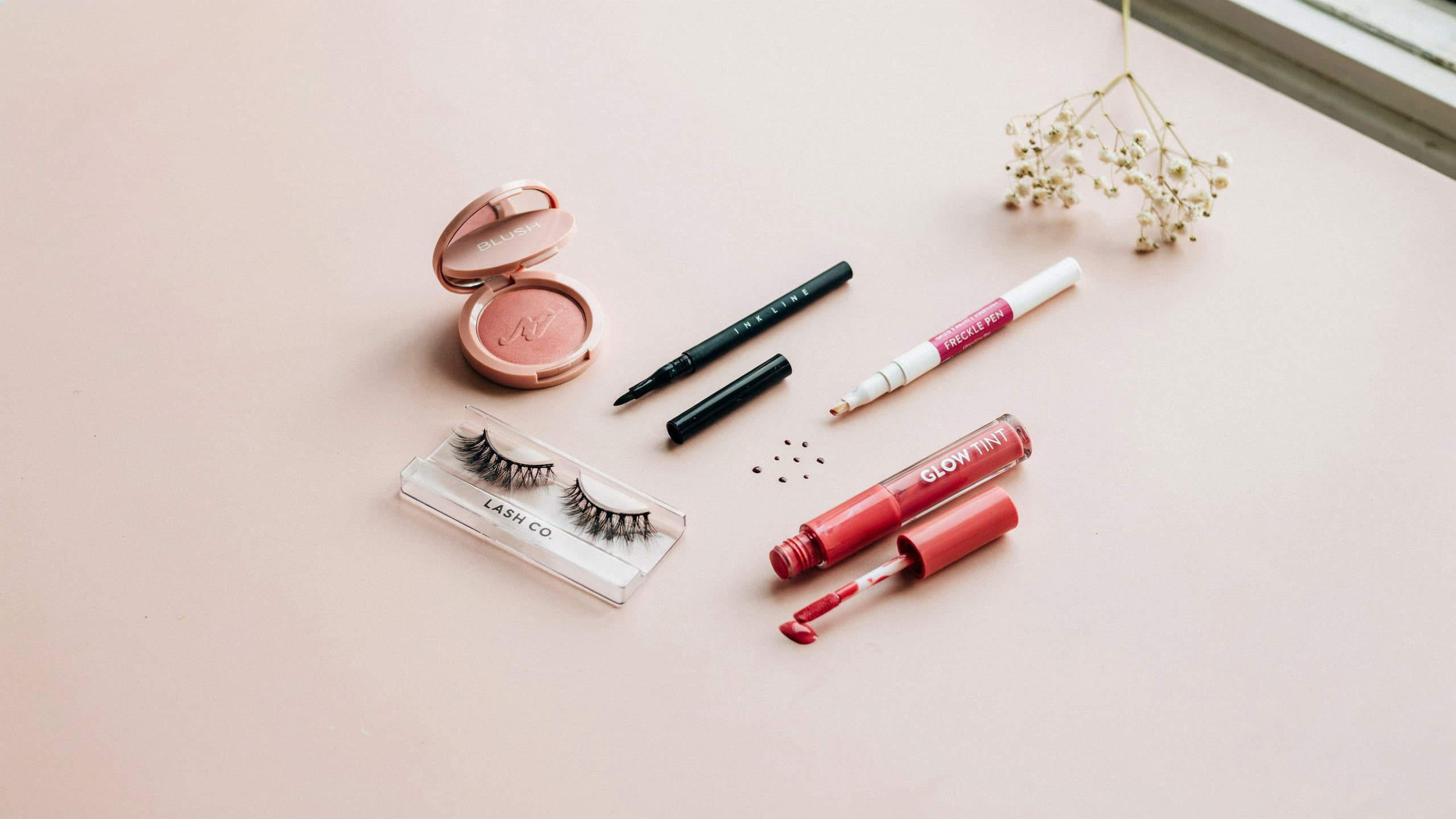 Egirl make up essentials products laid out flat on a solid light pink table