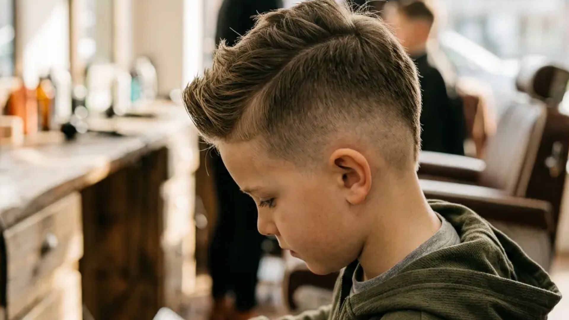 Boy with faux hawk fade hairstyle featuring sharp volume on top and clean faded sides in a modern salon setting.